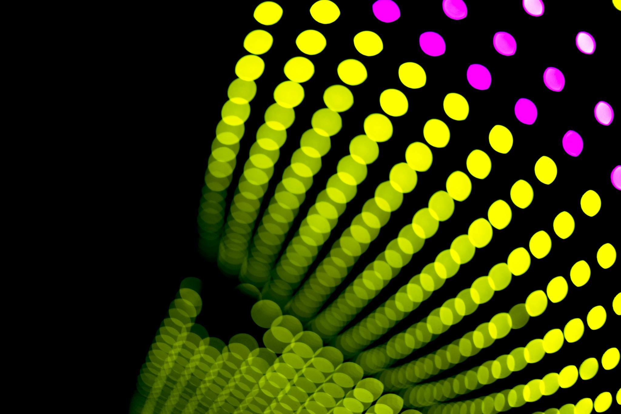 Colorful bokeh light patterns with vibrant yellow and pink hues on a black background.